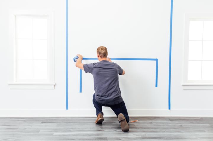 Homeowner preparing to install electric fireplace taping dimensions where unit will mount on the wall.