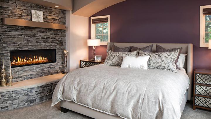 Heat & Glo Mezzo AU linear modern indoor gas fireplace with ribbon flame and amber glass on stone wall in master bedroom.