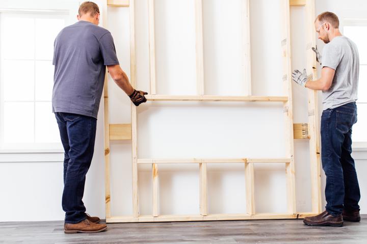 Homeowner and helper placing framed chase on wall where electric fireplace will be installed.