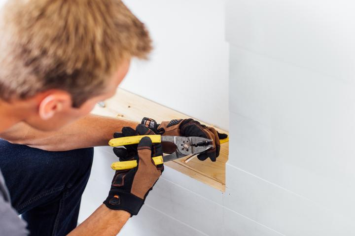 Homeowner with pliers separating wires to prepare for connecting electric fireplace to power source.