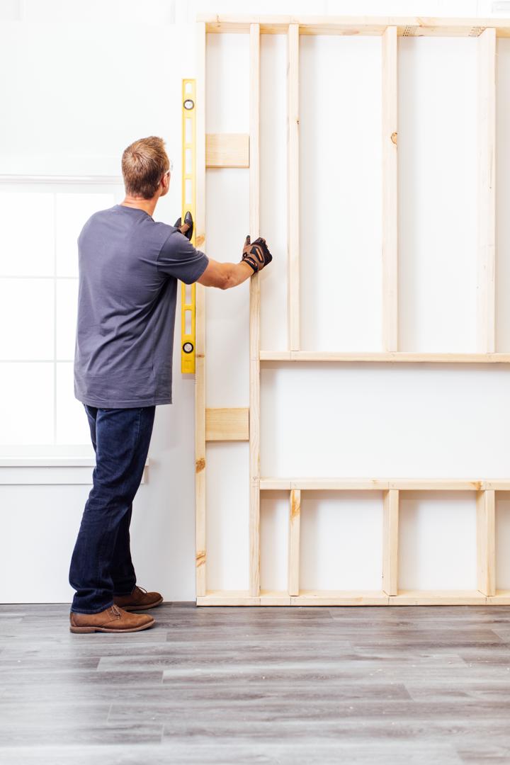 Homeowner checking with level whether framed chase is correctly positioned on wall for electric fireplace installation.