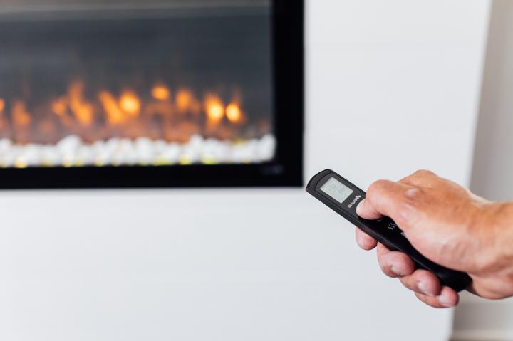 Homeowner using remote control to turn on newly installed linear electric fireplace.