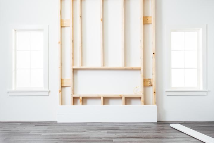 Framed wood chase with bottom plank of shiplap installed on wall for placement of linear electric fireplace.