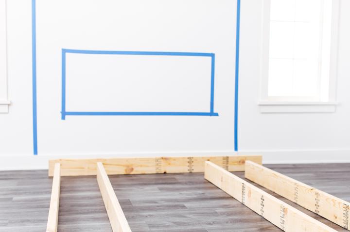 Electric fireplace framing wood on floor beneath wall where fireplace is marked with tape to be installed.