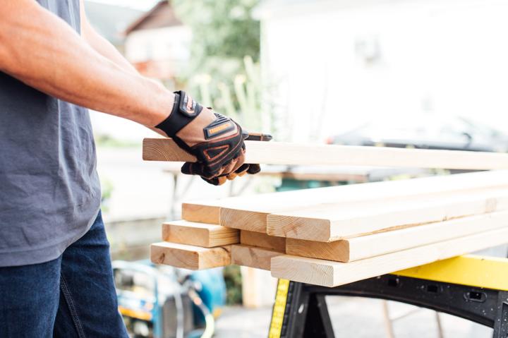 Homeowner with work gloves selecting a piece of framing wood for installing electric fireplace.