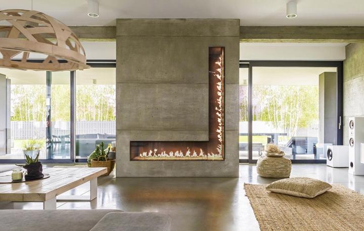 Custom L-shaped gas fireplace in concrete wall is centerpiece of boho space with nature views. 